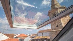 Finestra amb lucerna que mostra una torre històrica i edificis circumdants.