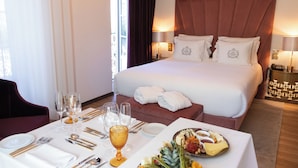 Habitació d'hotel amb un llit gran, una taula de menjador preparada per a dues persones i una safata de petitdejuni amb diversos aliments.