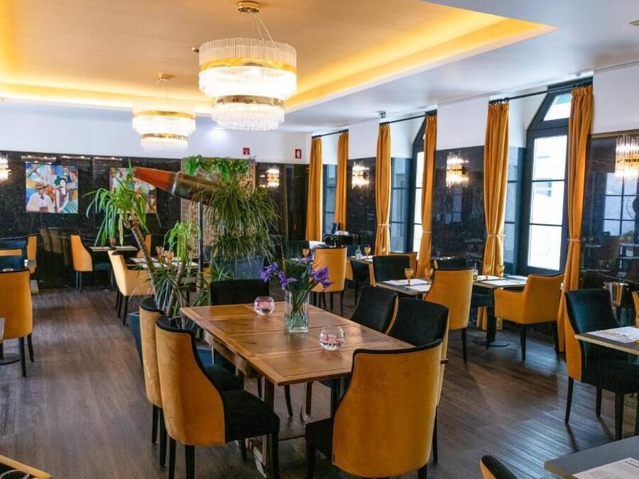 A restaurant with wooden tables, yellow chairs, and large windows with curtains.