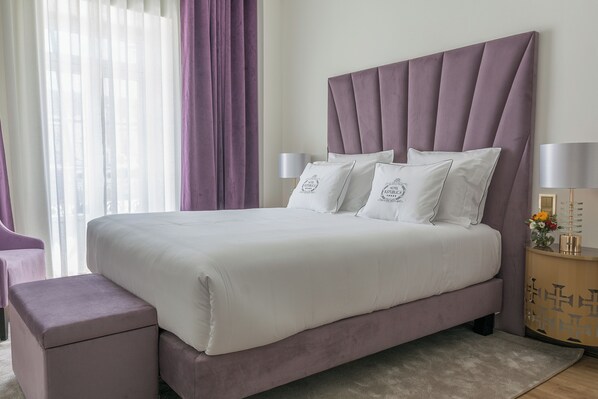 Una cama bien hecha con cabecera, dos lámparas de noche y una mesita de noche con un jarrón de flores.