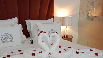 A hotel room with a bed, pillows, a red headboard, a nightstand with a lamp, and a wall with a decorative item.