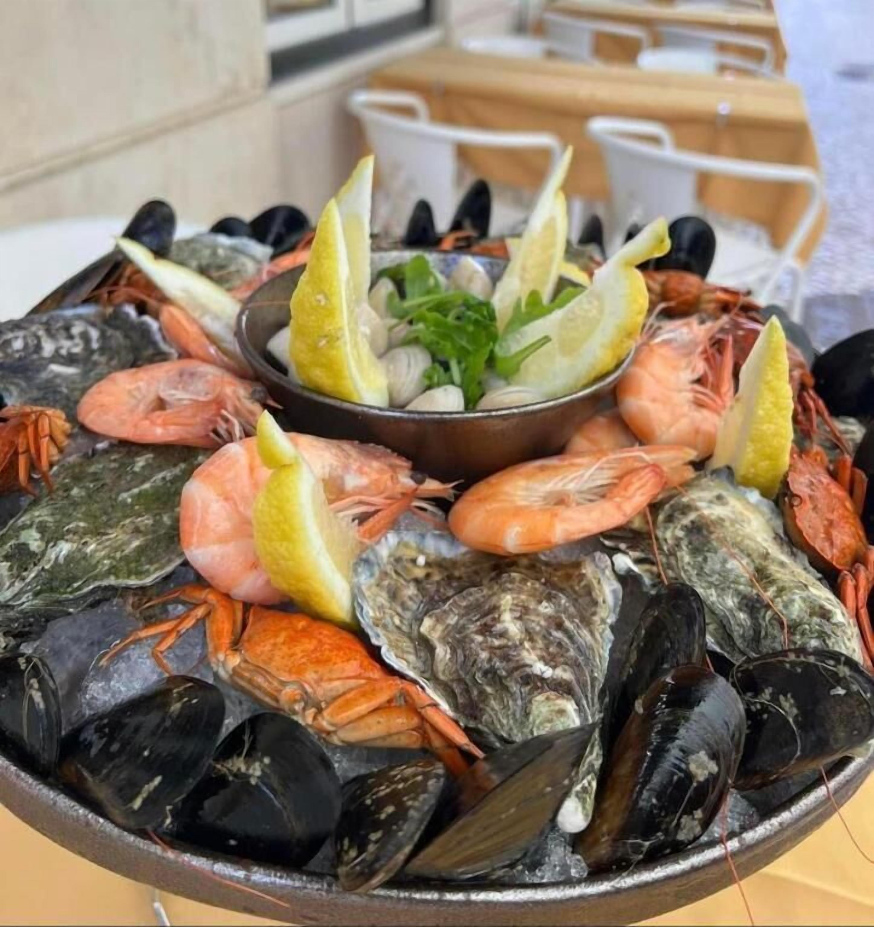 Un plateau de fruits de mer comprenant divers crustacés et crevettes, agrémenté de tranches de citron et d’herbes aromatiques, présenté sur une table.