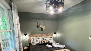 Ein Schlafzimmer mit Bett, einem Fenster mit Vorhängen, einer Hängeleuchte und einem Deckenventilator.