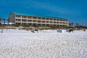 Ein mehrstöckiges Hotel mit flachem Dach und Balkonen, gelegen an einem Sandstrand mit Dünen im Hintergrund.