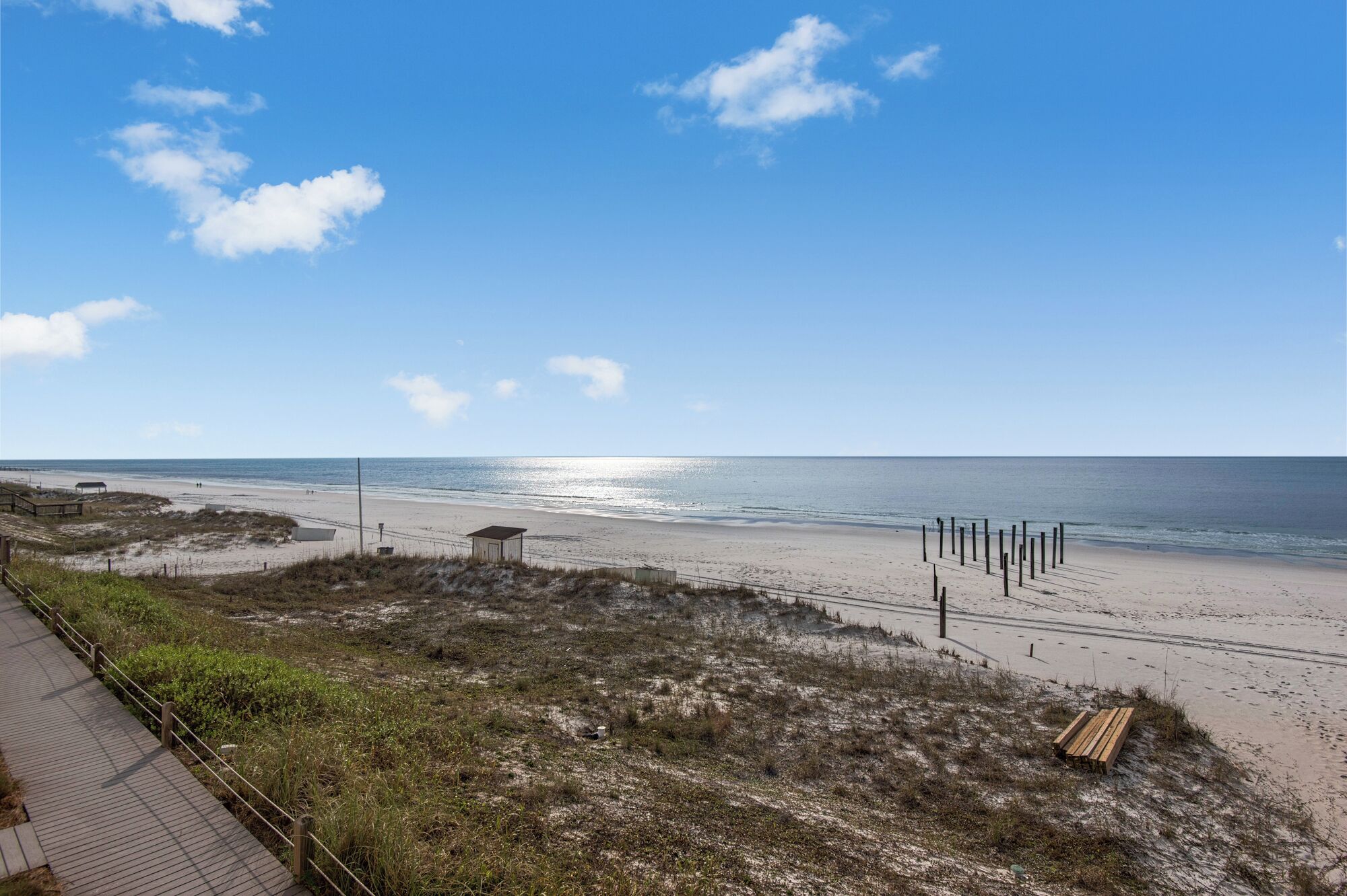 A beach with a wooden walkway, a small shelter, and a wooden bench.
