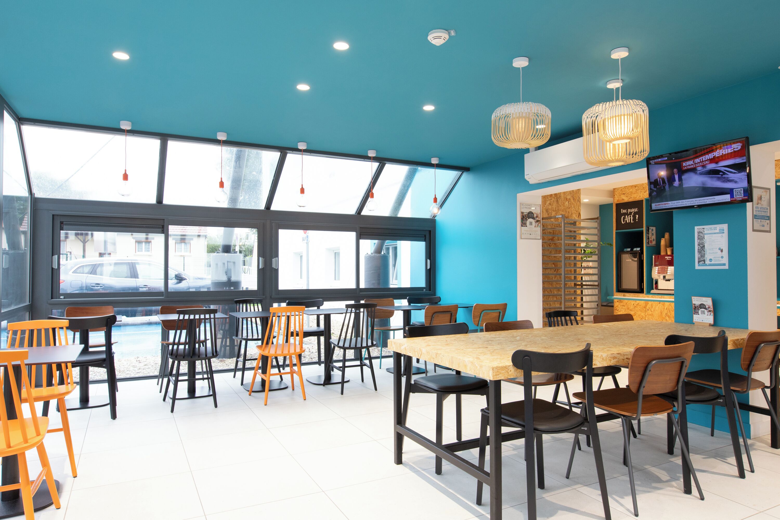 A modern cafe with large windows, a wooden table, and multiple chairs.