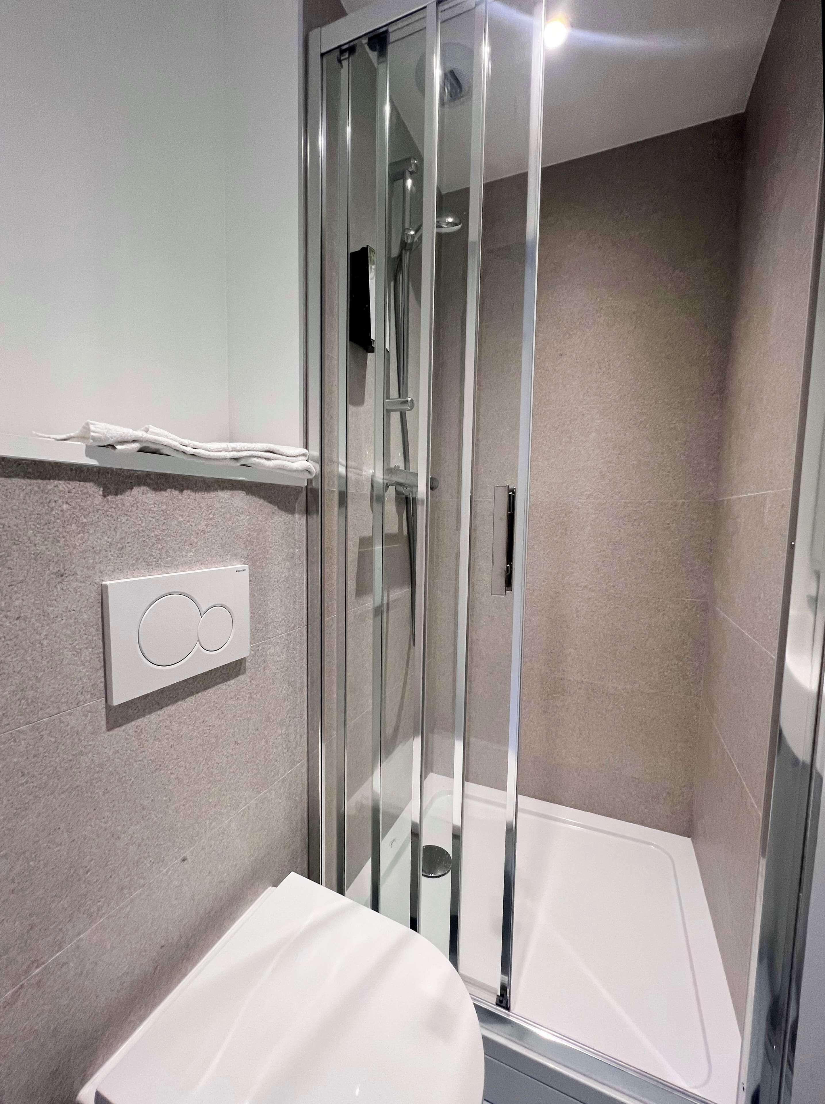 A modern bathroom with a glass-enclosed shower, a white toilet, and a wall-mounted control panel.