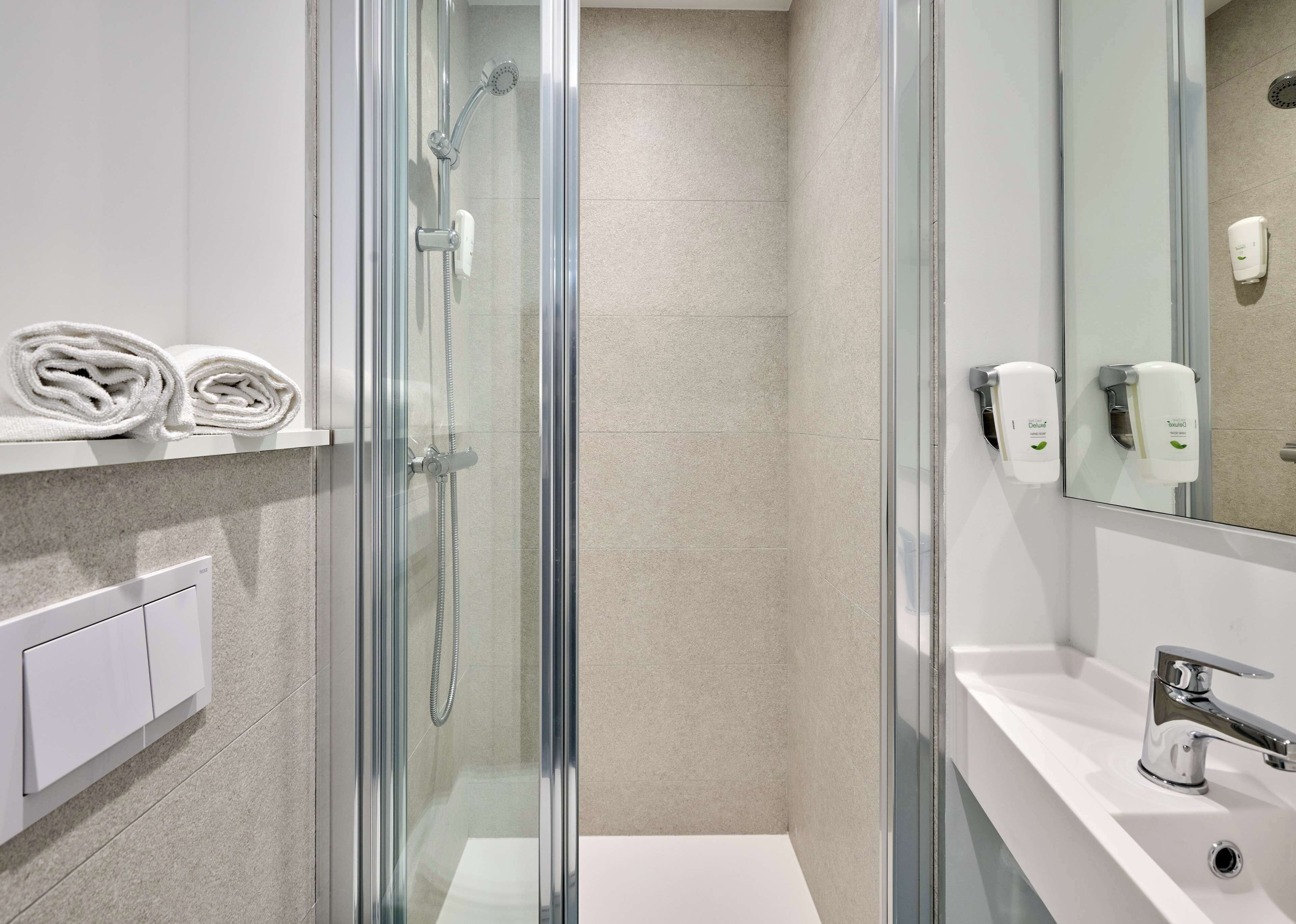 Een moderne badkamer met een douchecabine van glas, een wit wastafelmeubel en zeepdispensers.