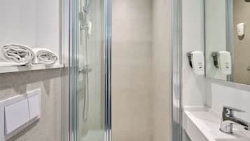 Een moderne badkamer met een douchecabine van glas, een wit wastafelmeubel en zeepdispensers.
