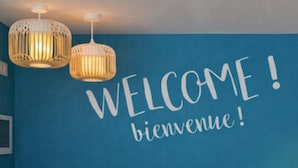 A reception area with a blue wall, a 'WELCOME' sign, and two pendant lights. - Kyriad ECO - Nevers Nord Varennes Vauzelles (Varennes-Vauzelles)