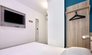 A modern hotel room with a bed, a mounted TV, a wooden wardrobe, and a hanging black hanger.