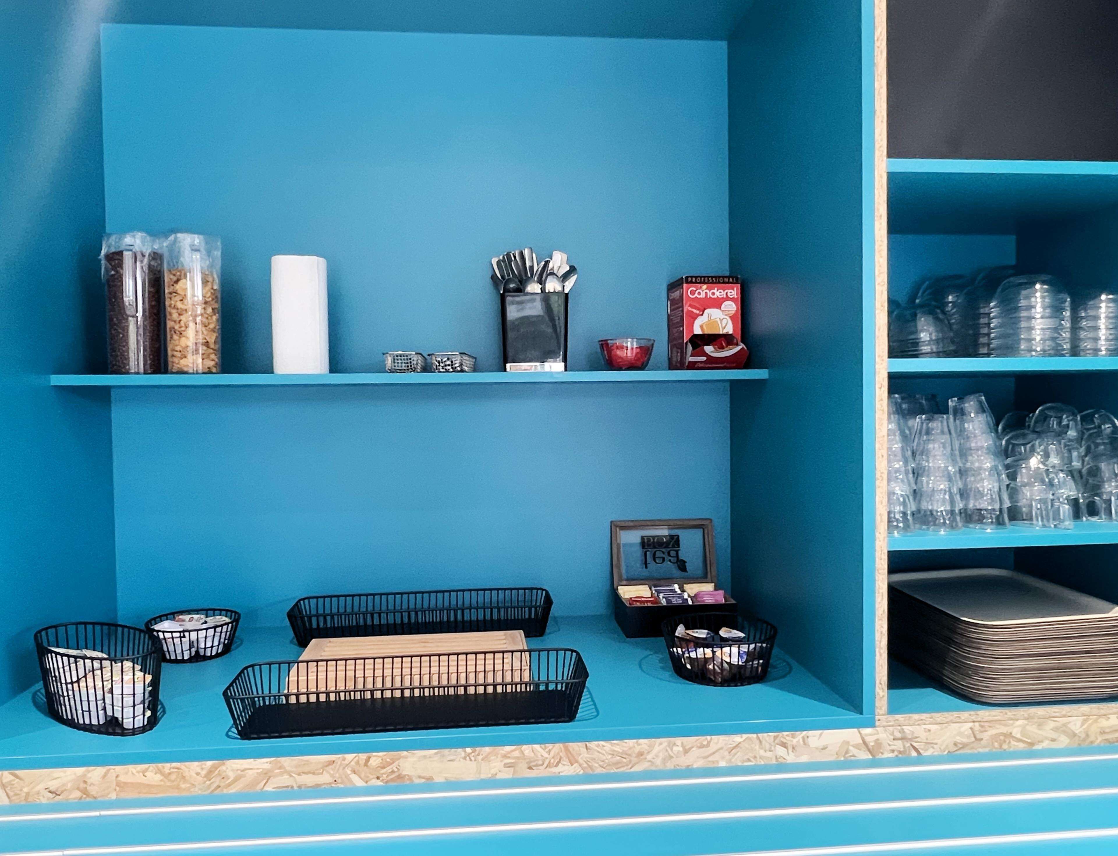 A blue-themed room with shelves holding various items like containers, a box, and a framed picture.