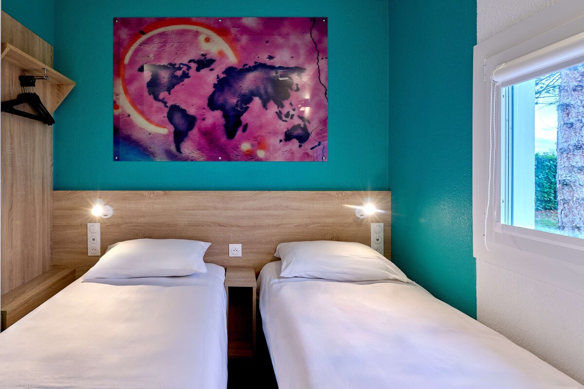 Une chambre avec deux lits, une tête de lit en bois, une décoration murale représentant une carte du monde et une fenêtre donnant sur des arbres.