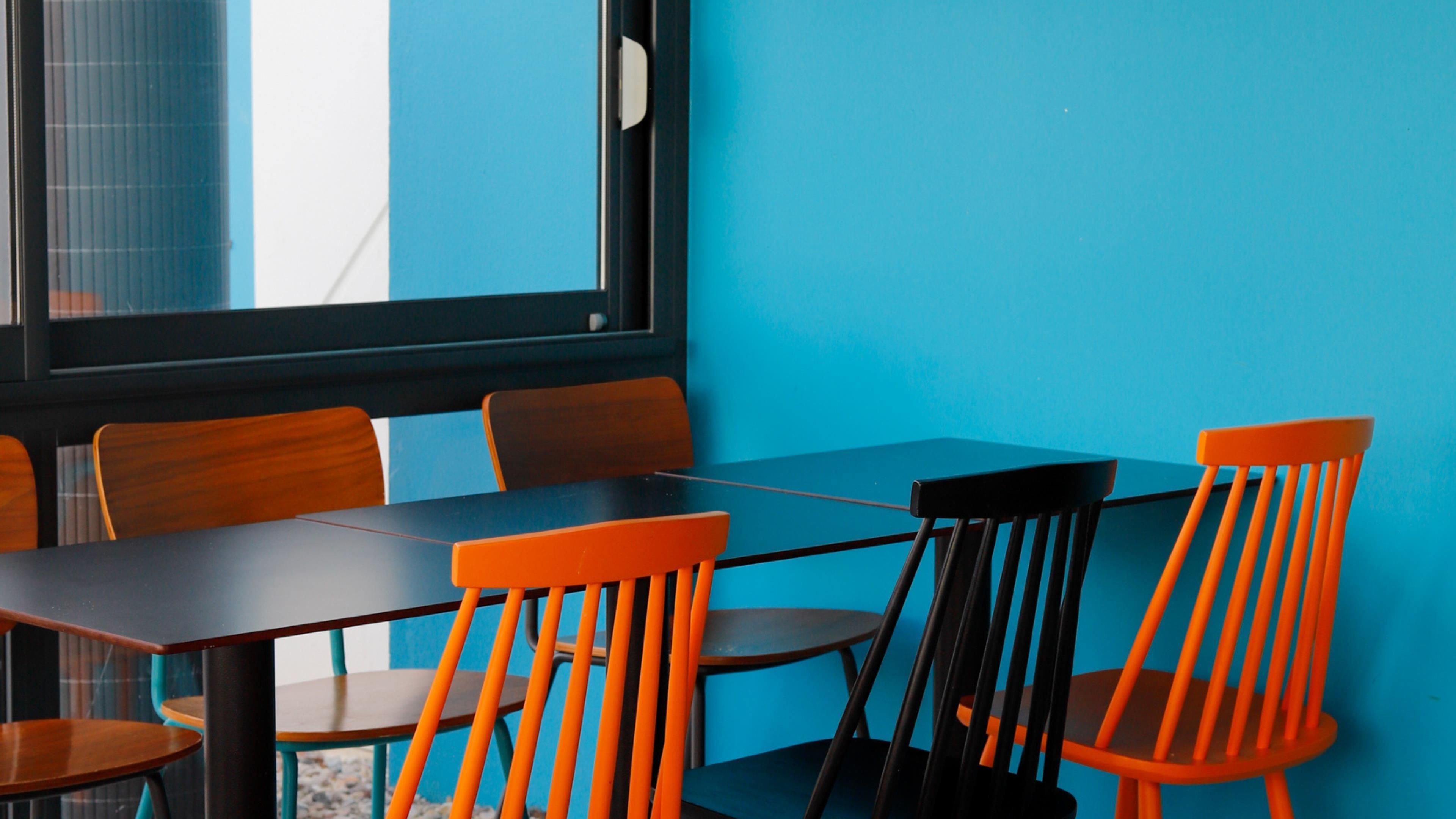 Una habitación con pared azul, una mesa negra y sillas de madera.