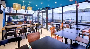 An indoor dining area with tables and chairs, large windows, and hanging light fixtures.