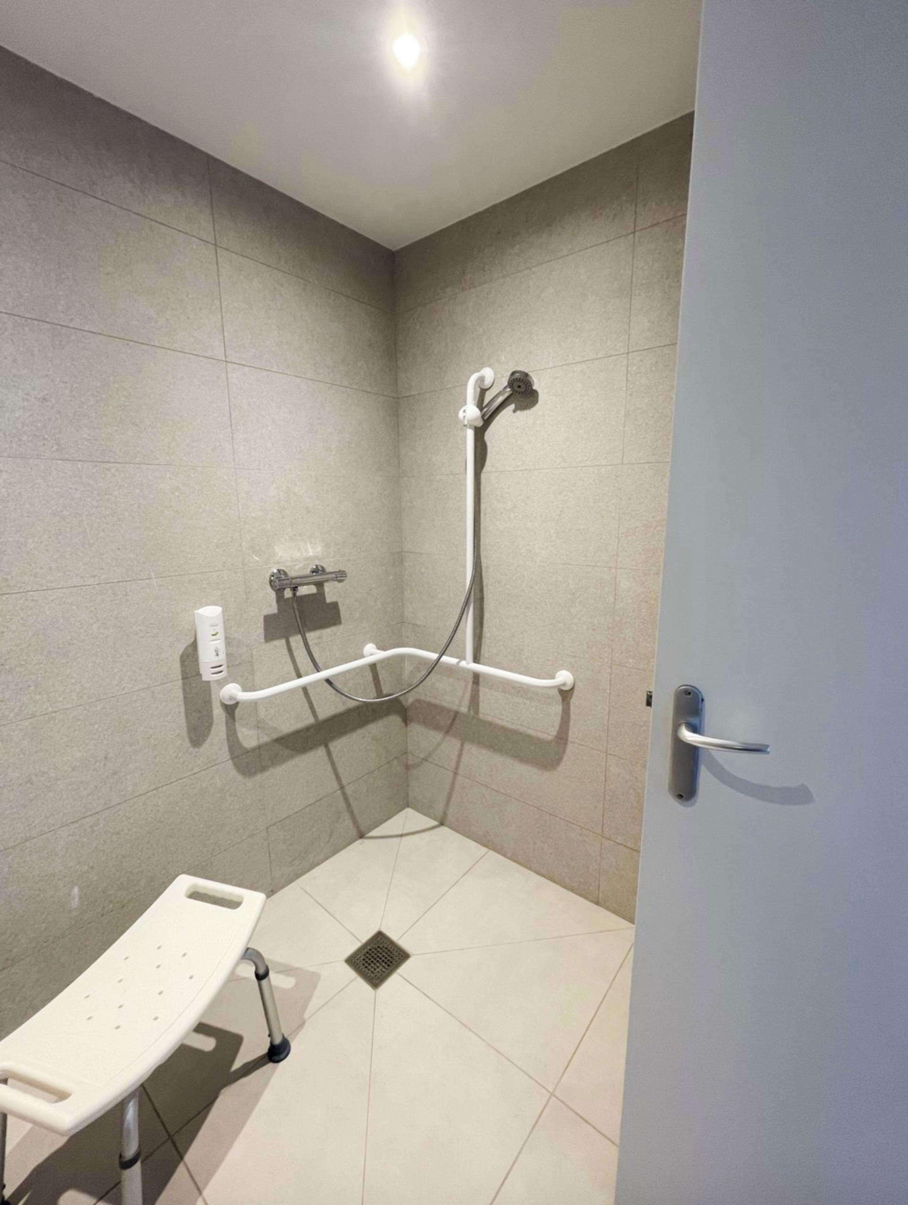 A bathroom with a shower, grab bars, a toilet, and a door.