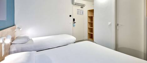 Habitación de hotel con dos camas individuales, un armario, un equipo de aire acondicionado y una puerta con manija.
