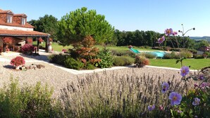 A house with a covered patio, a swimming pool, and a well-maintained garden with various plants and flowers.