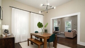 Un coin repas avec une table en bois, des chaises et un banc. On peut voir une plante sur la table, une lampe sur une table d’appoint et un téléviseur au fond.