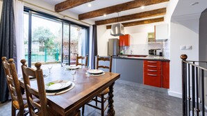 Un coin repas avec une table et des chaises en bois, une cuisine avec des placards rouges et une porte-fenêtre coulissante donnant sur un jardin.