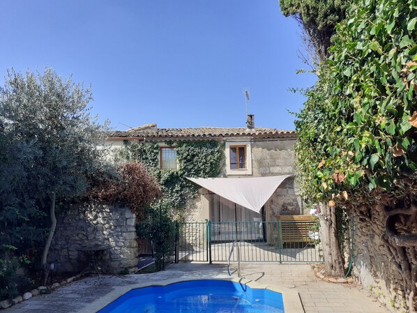 A stone house with a swimming pool, surrounded by greenery and a stone wall.