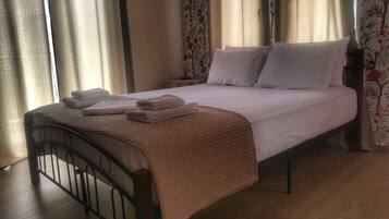 A neatly made bed with white linens and a beige blanket, a wooden headboard, and floral curtains.