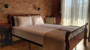Una cama bien hecha con cabecera de madera, una mesita de noche con lámpara y una pared de ladrillo.