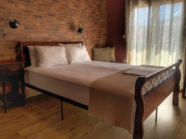 Una cama bien hecha con cabecera de madera, una mesita de noche con lámpara y una pared de ladrillo.