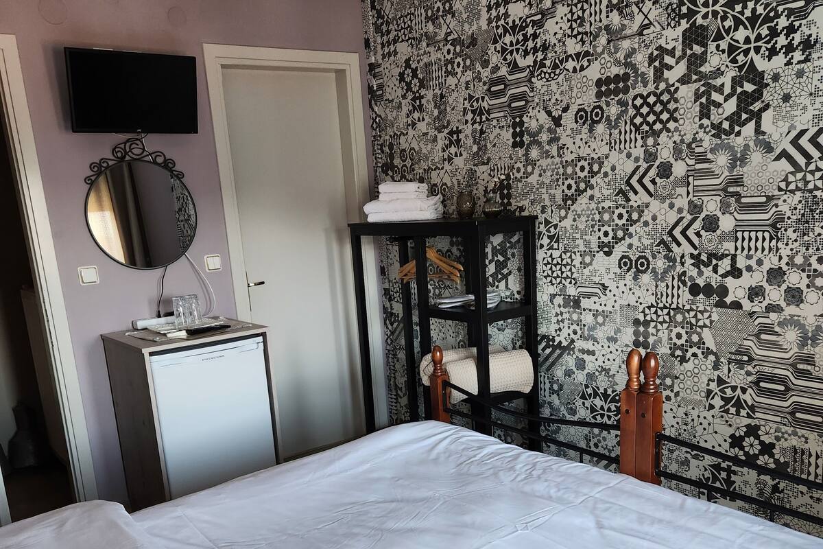 A bedroom with a large bed, a dresser, a mirror, a wall-mounted TV, and a patterned wallpaper.