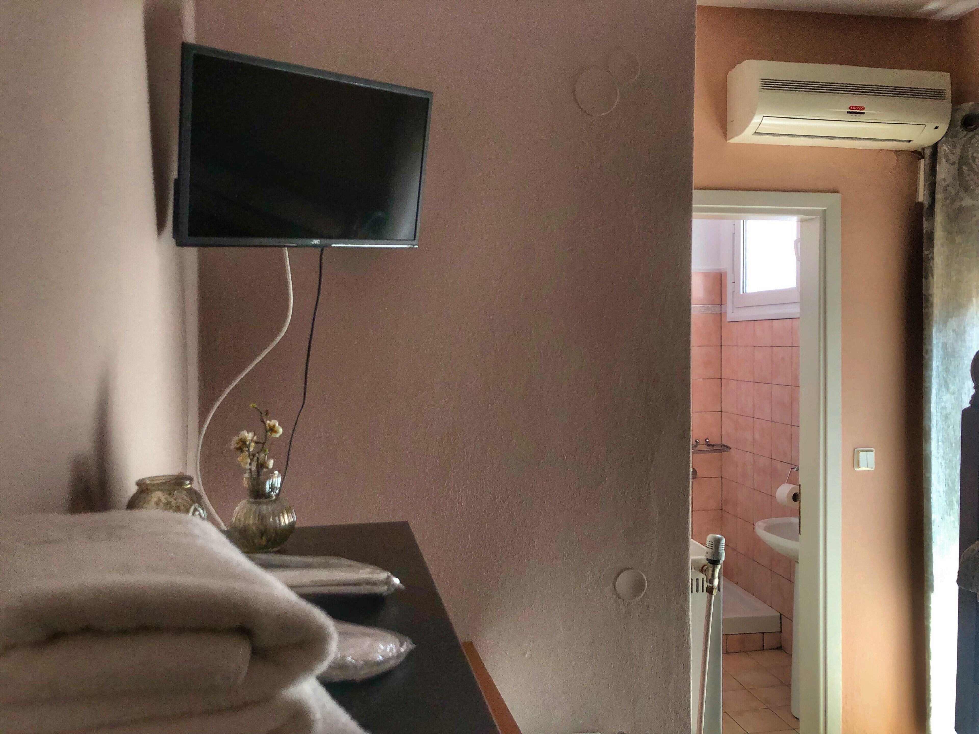 Un bagno con lavandino, water e doccia. C'è una televisione montata a parete e un portasciugamani con asciugamani.