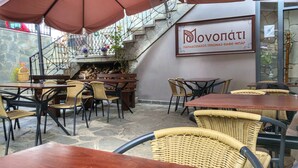 Un café al aire libre con mobiliario de mimbre, suelo de piedra y una escalera que lleva a un nivel superior.