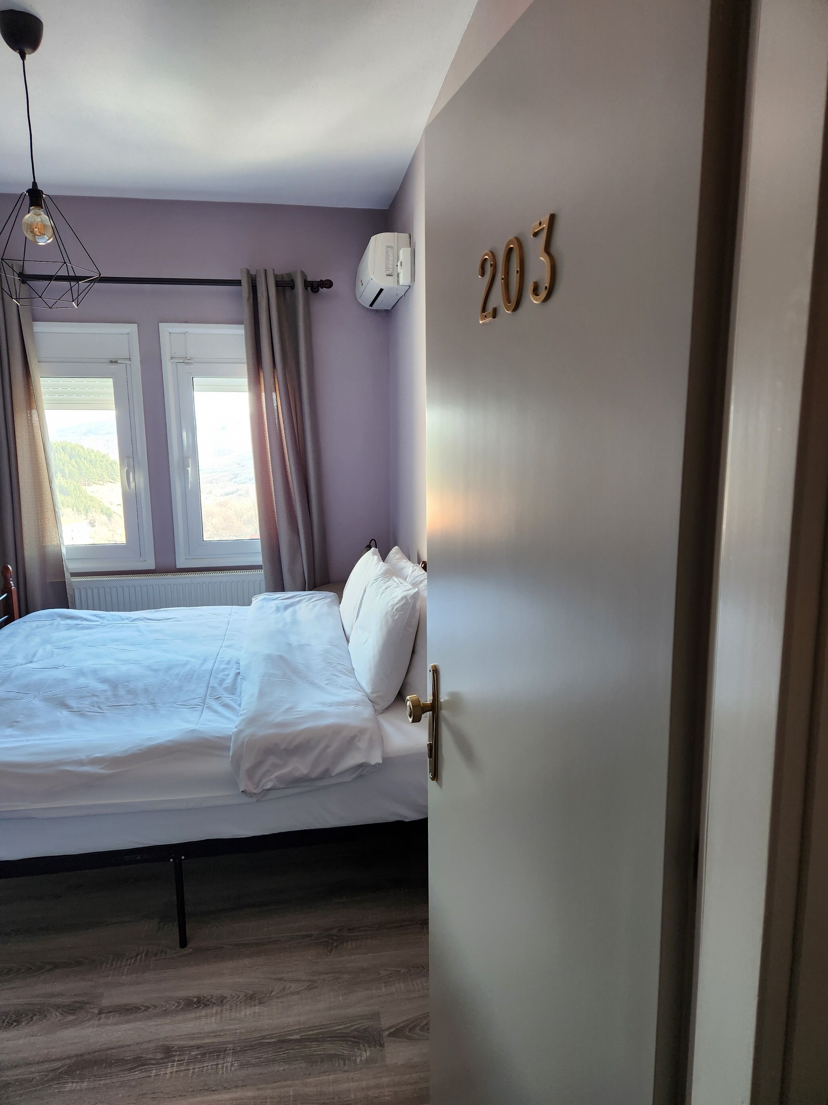 A bedroom with a bed, a window, a wall-mounted air conditioner, and a door with the number 203.