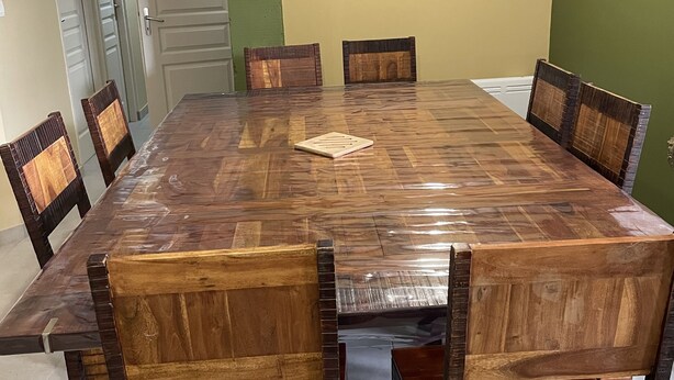 Un espace repas avec une grande table en bois entourée de chaises, un luminaire suspendu et une porte visible au fond.