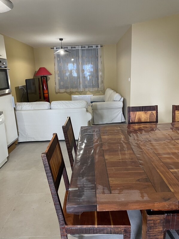 A dining area with a wooden table and chairs, a sofa, a TV, and a lamp.