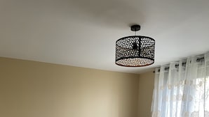 Une chambre avec deux lits, un luminaire au plafond et une fenêtre ornée de rideaux légers.