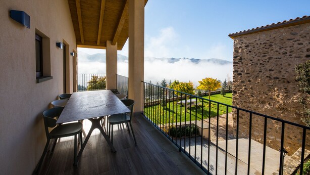 A balcony with a table and chairs, overlooking a garden and a stone building. - DALT'S COUNTRY (Sant Joan de les Abadesses)