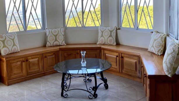 A corner seating area with a round table, large windows with yellow curtains, and patterned cushions.