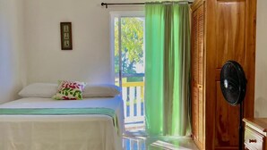 A bedroom with a bed, a wooden wardrobe, a fan, and a view of the outside.