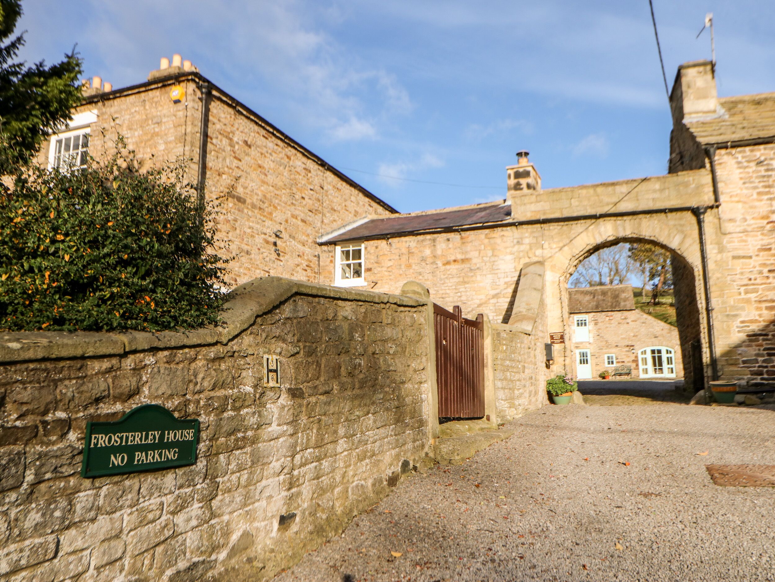 A stone building with a 'No Parking' sign, an archway entrance, and a small garden area.