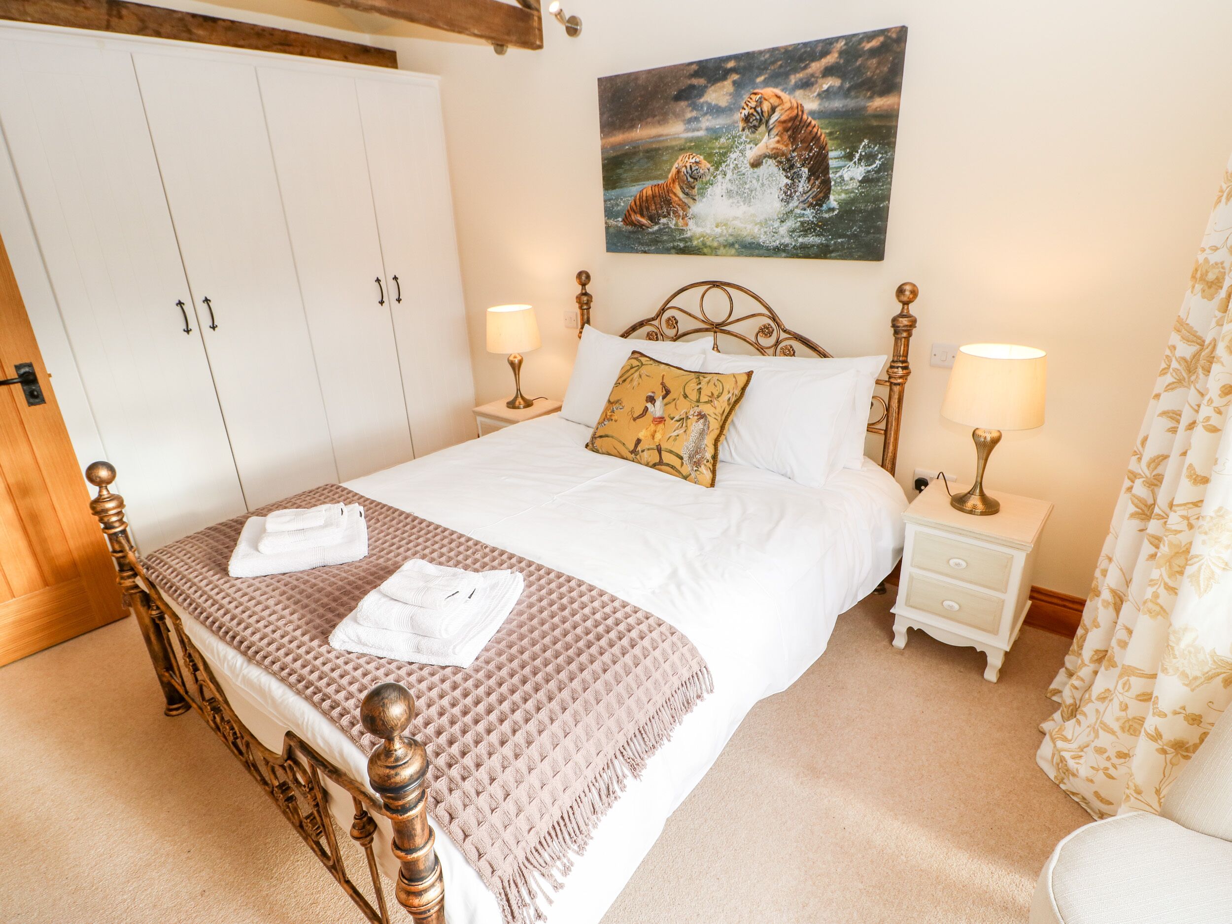 A bedroom with a large bed, two bedside tables, a wardrobe, and a painting of tigers.