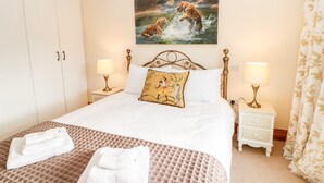 A bedroom with a large bed, two bedside tables with lamps, a wardrobe, and a painting of tigers on the wall. - The Coach House (Bishop Auckland)