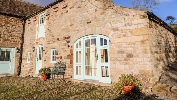 A stone building with a cobblestone courtyard, a bench, and potted plants. - The Coach House (Bishop Auckland)