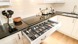 A modern kitchen with white cabinets, a black countertop, and a drawer organizer filled with utensils. - The Coach House (Bishop Auckland)
