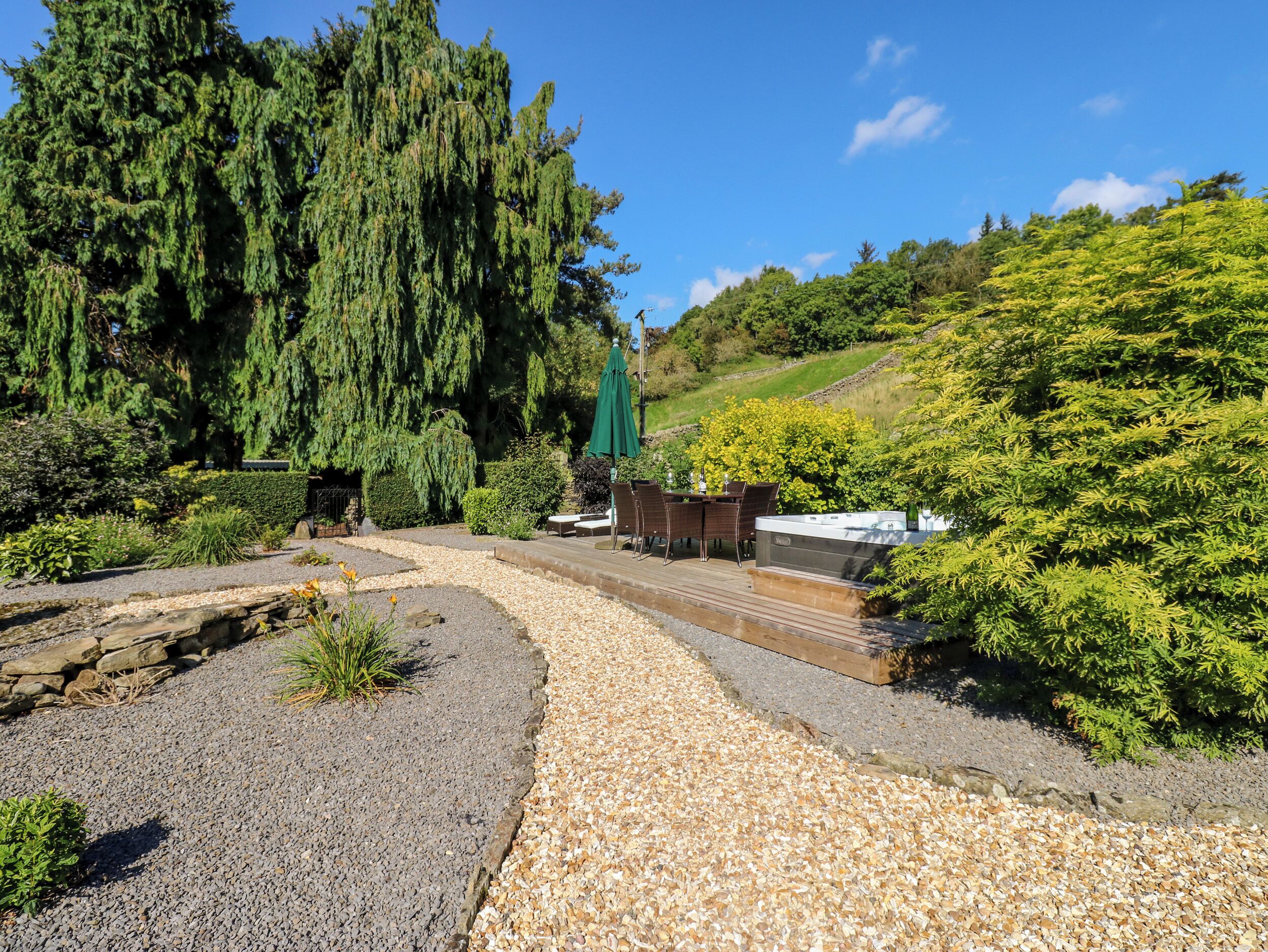 Un jardín con terraza de madera, un jacuzzi y un muro de piedra.