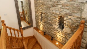A staircase with wooden railings, a stone wall, and a mirror reflecting the staircase. - The Barn (Bishop Auckland)