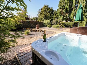 A hot tub with a bottle of champagne, surrounded by a garden with various plants and a stone wall. - The Barn (Bishop Auckland)