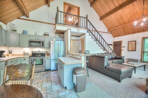 Cozy cabin-style home features a kitchen, dining area, and living space with a staircase leading to a balcony.