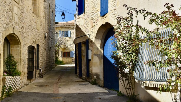 Une rue étroite bordée d’immeubles en pierre, avec des portes en arc de cercle et un portail bleu.