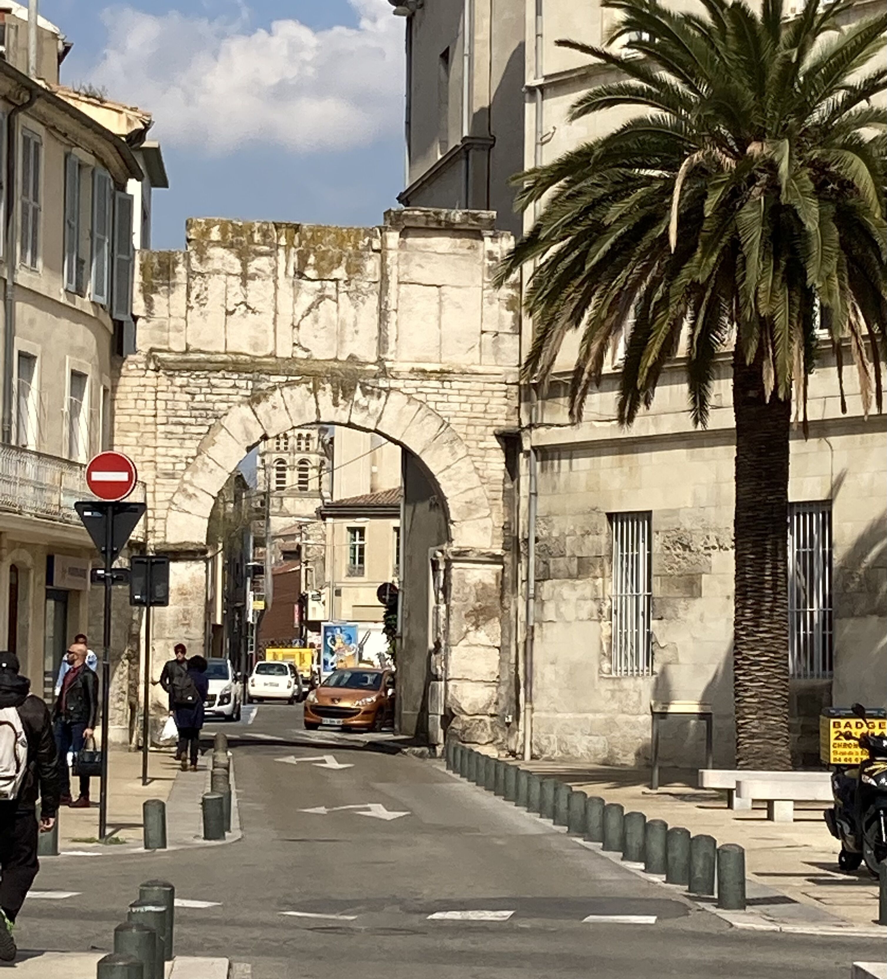 Une rue avec une arche en pierre, des palmiers et un panneau indiquant l’interdiction d’accès.