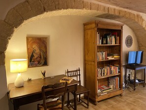 A study room with a wooden desk, a bookshelf, a lamp, and a framed painting.